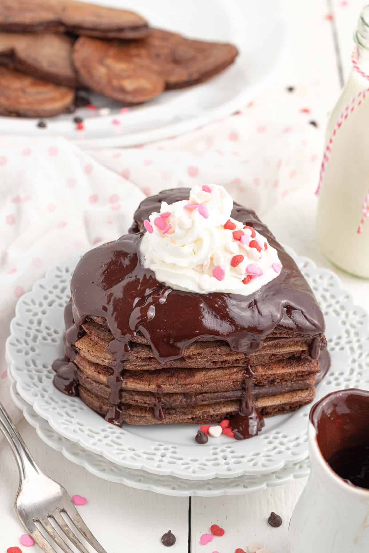 Stack of pancakes in the shape of a heart, with whipped cream and sprinkles.