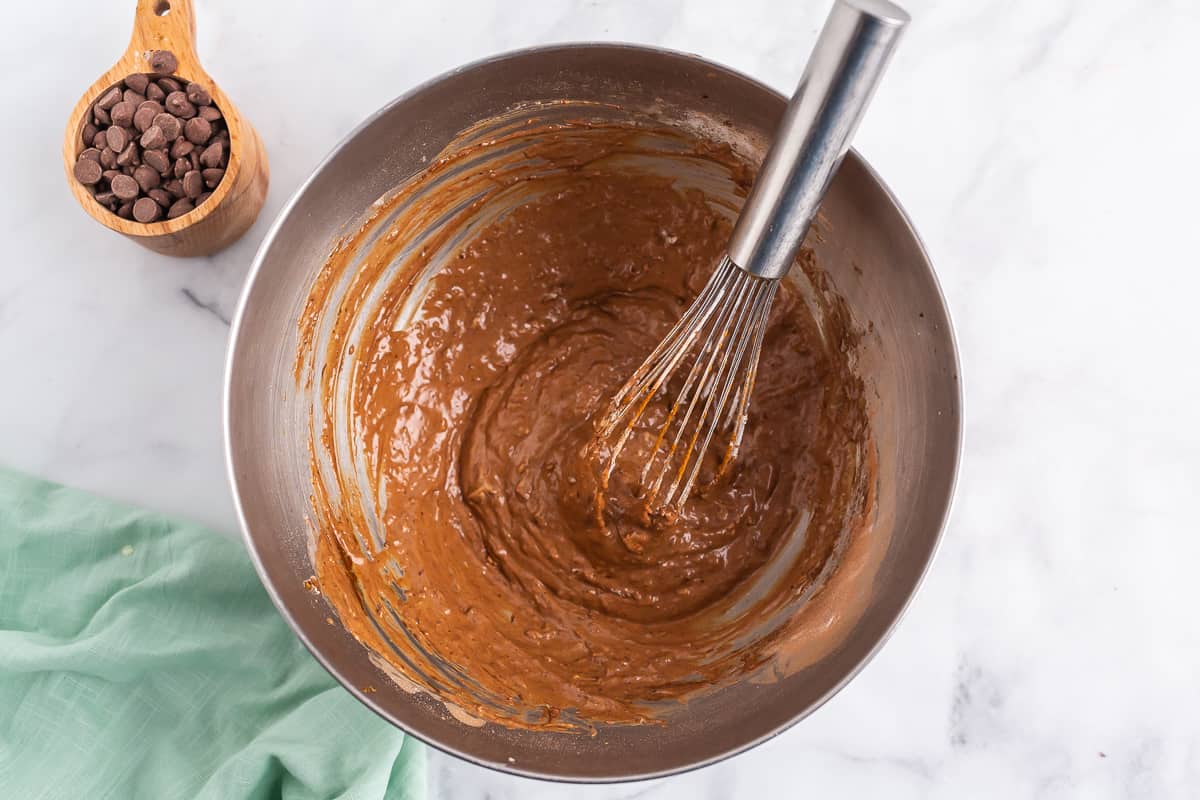 Chocolate pancake batter and silver whisk in a stainless steel mixing bowl.