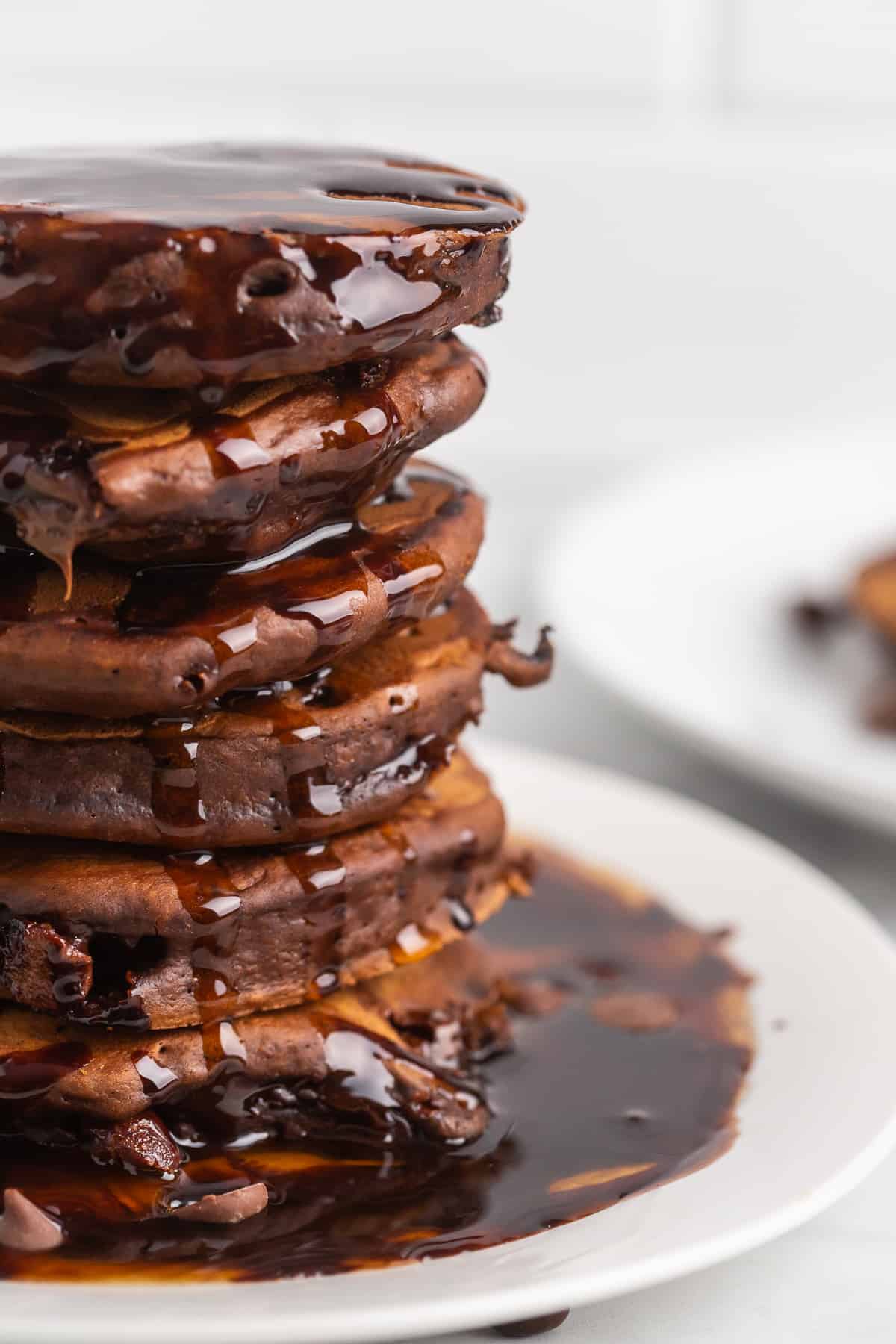 Close up of tall stack of chocolate pancakes with chocolate syrup.