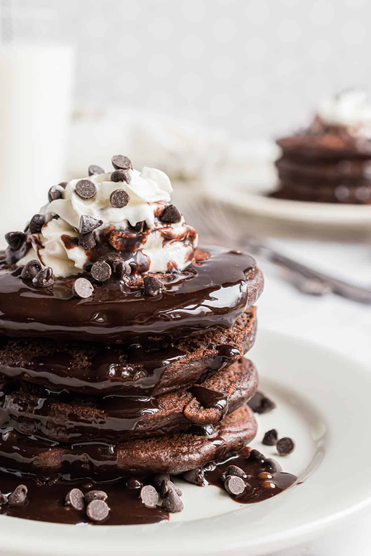 Stack of chocolate pancakes topped with whipped cream, chocolate chips, and chocolate syrup.