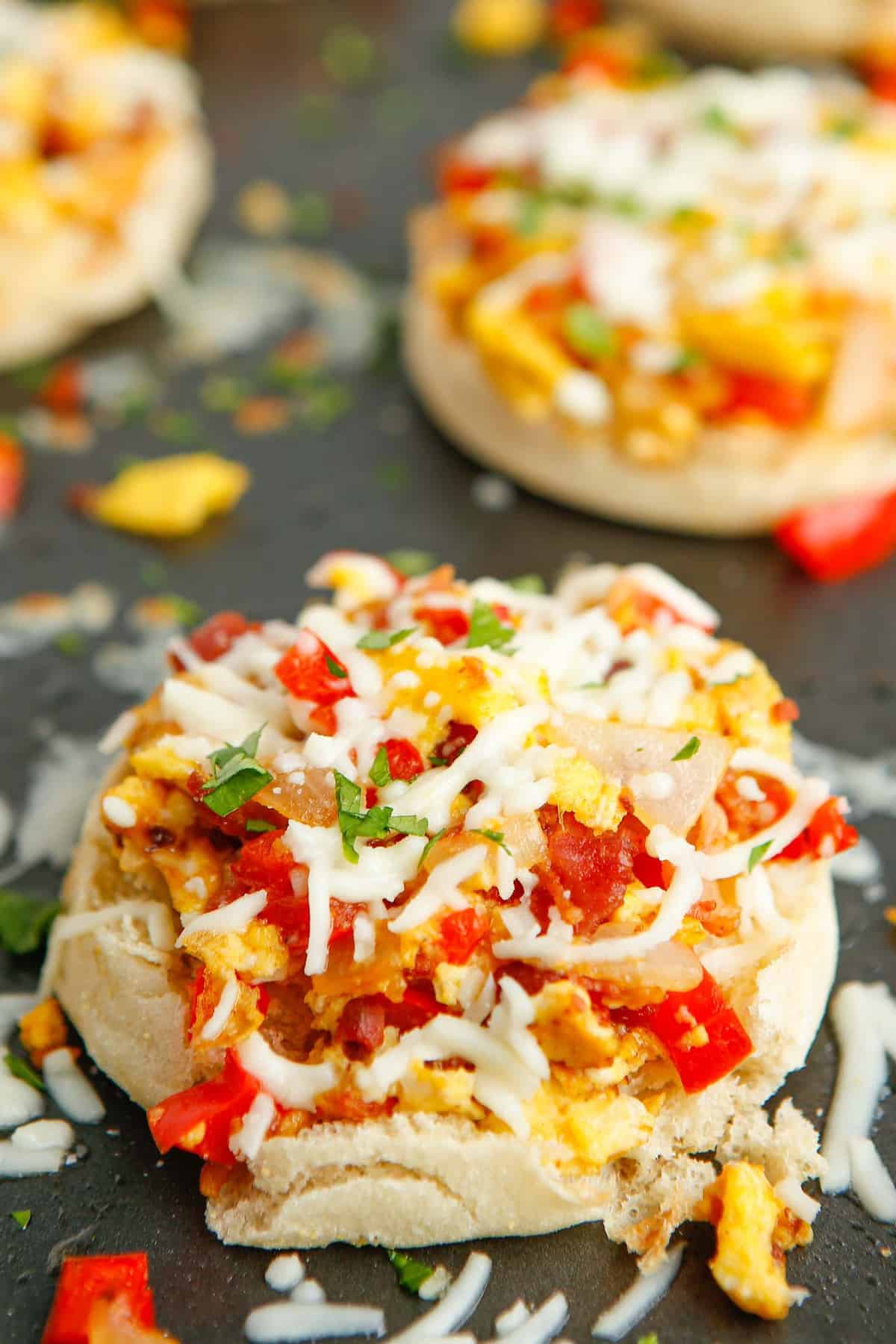 Close up view of an english muffin breakfast pizza with peppers and bacon.
