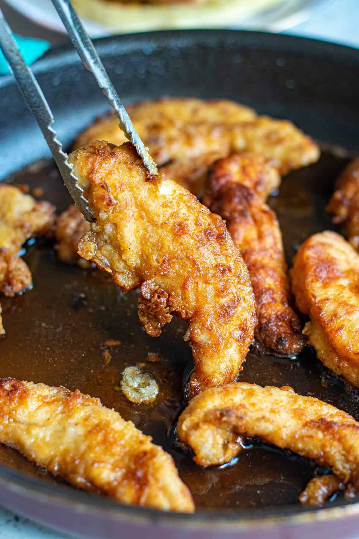 Fried chicken being taken out of a pan on tongs.