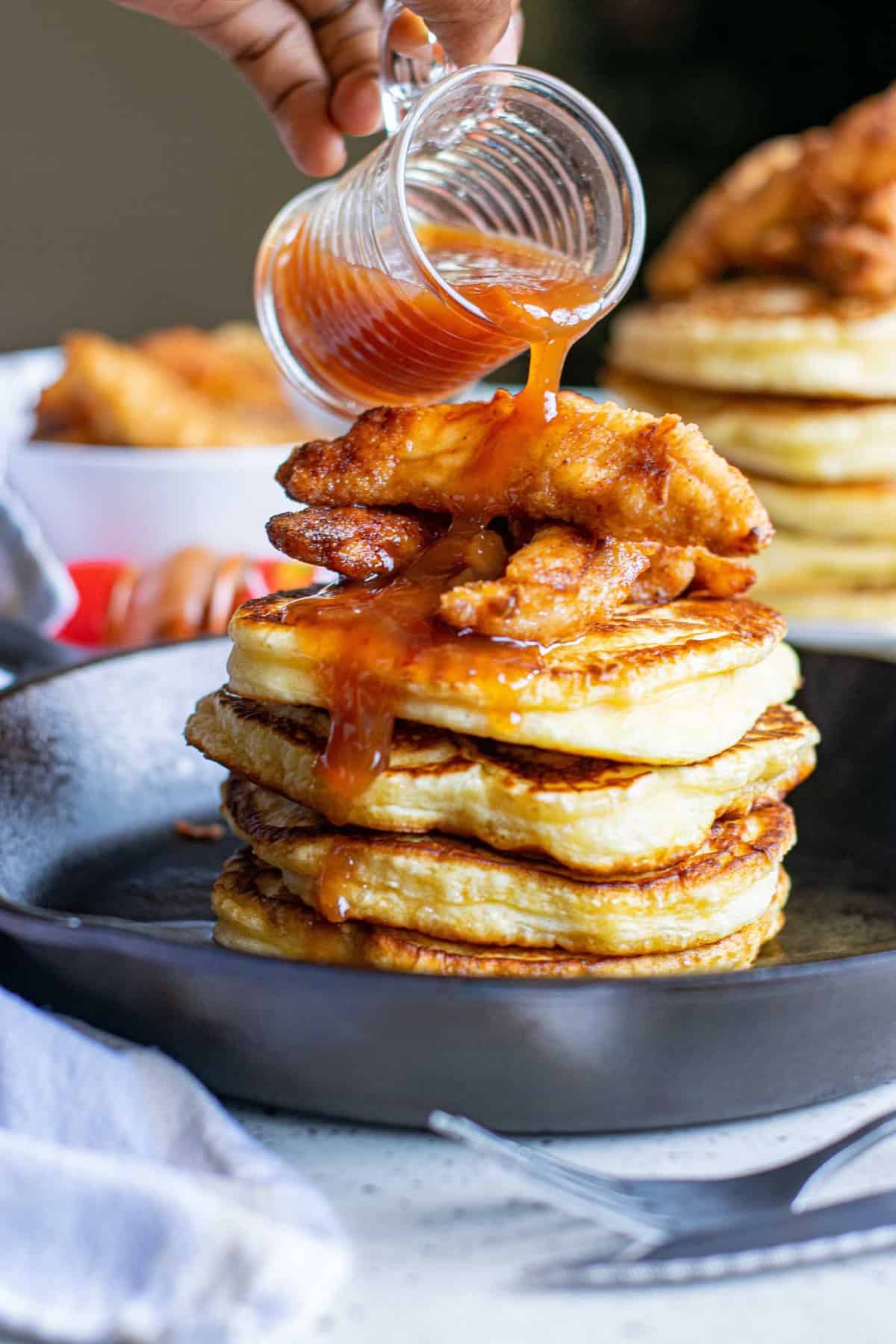 Sriracha maple sauce being poured on a stack of pancakes.