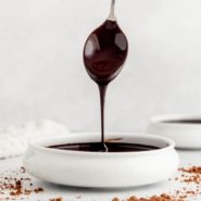 Chocolate syrup dripping off a spoon into a small bowl.