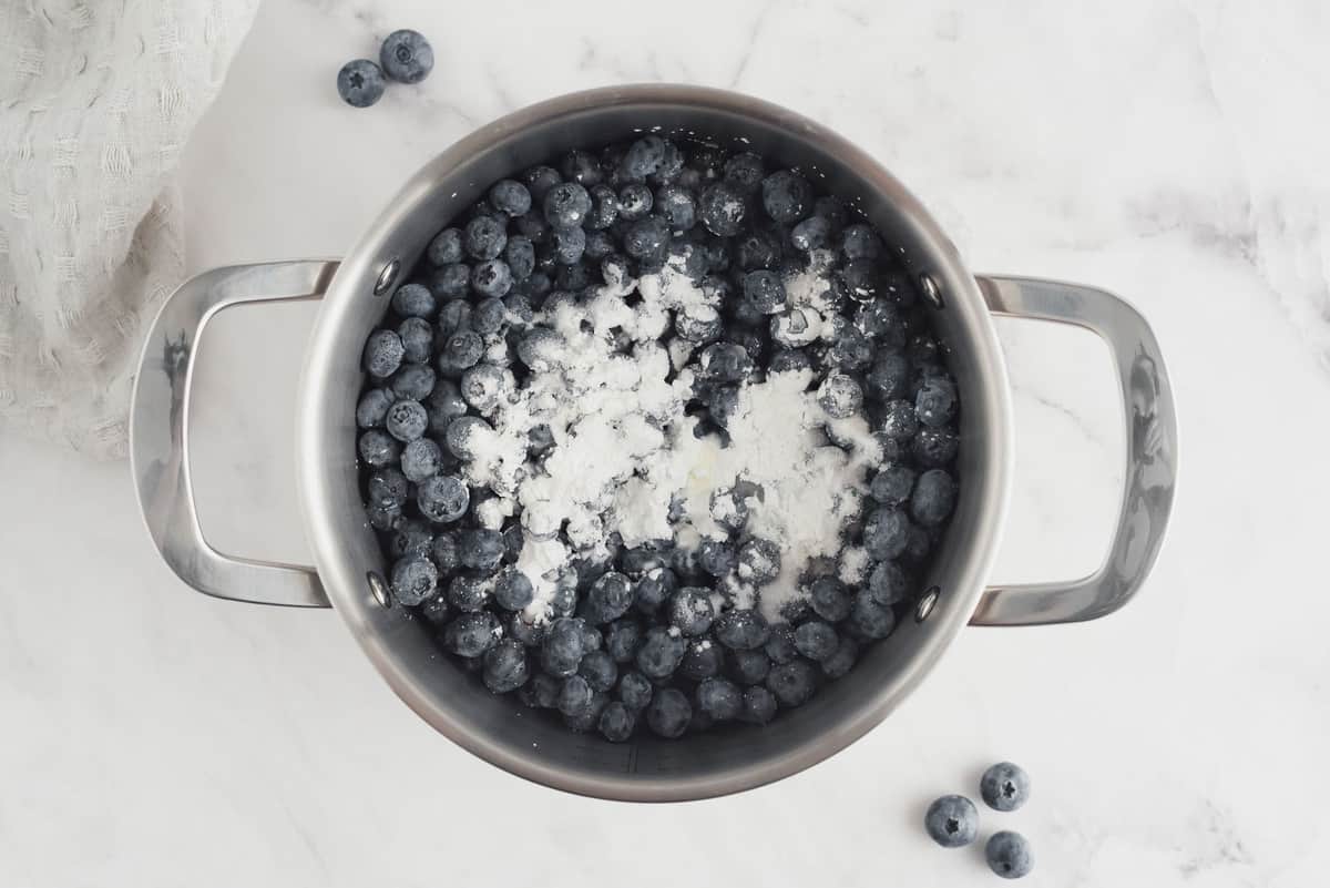 Ingredients for blueberry sauce in a saucepan with two handles.