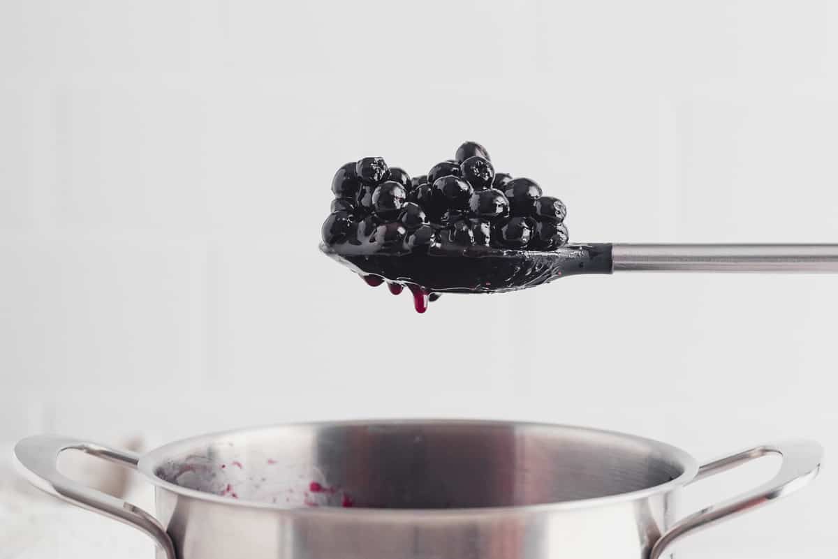 Spoon of blueberry sauce hovering over a pan.