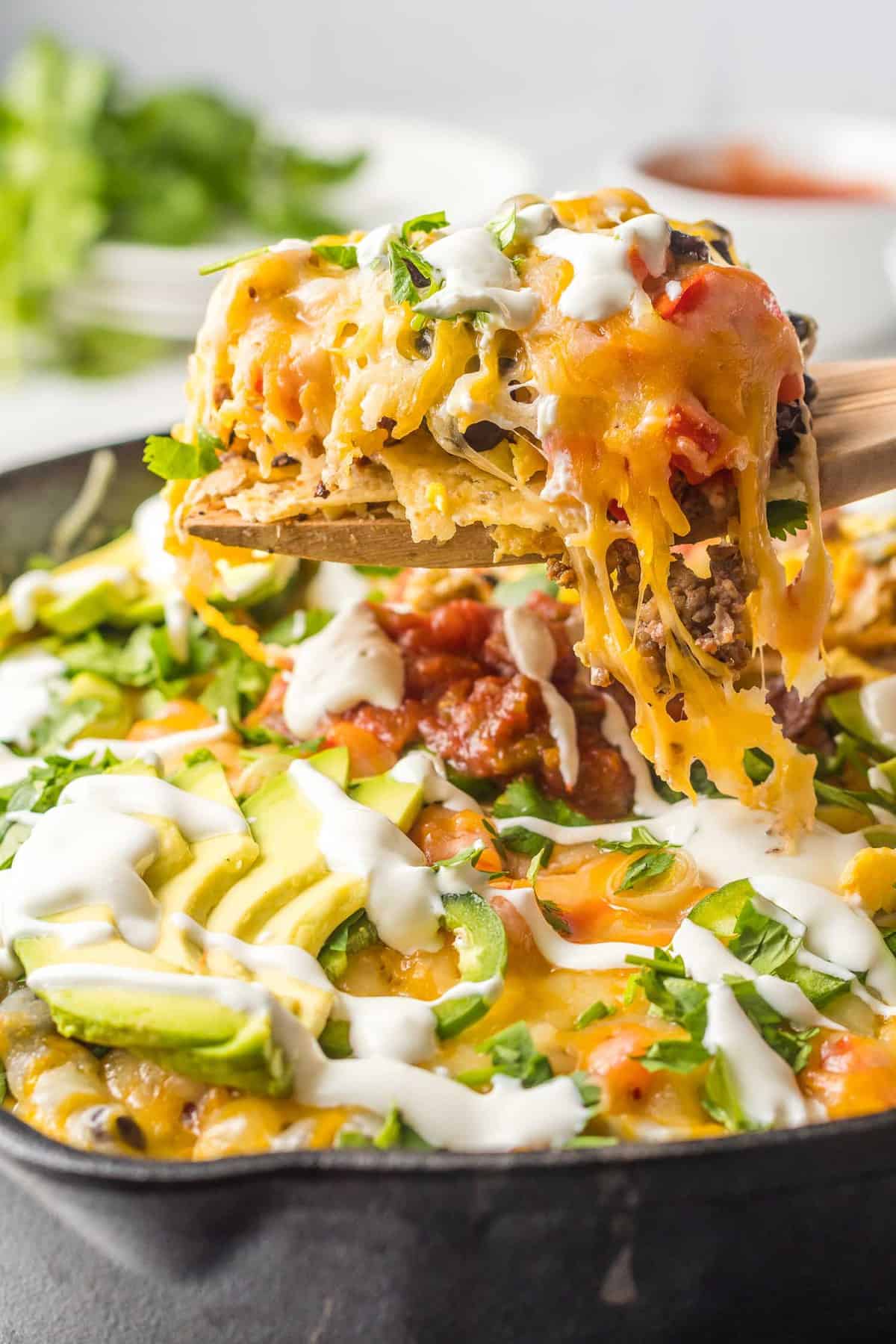Nachos being scooped out of a cast iron pan.