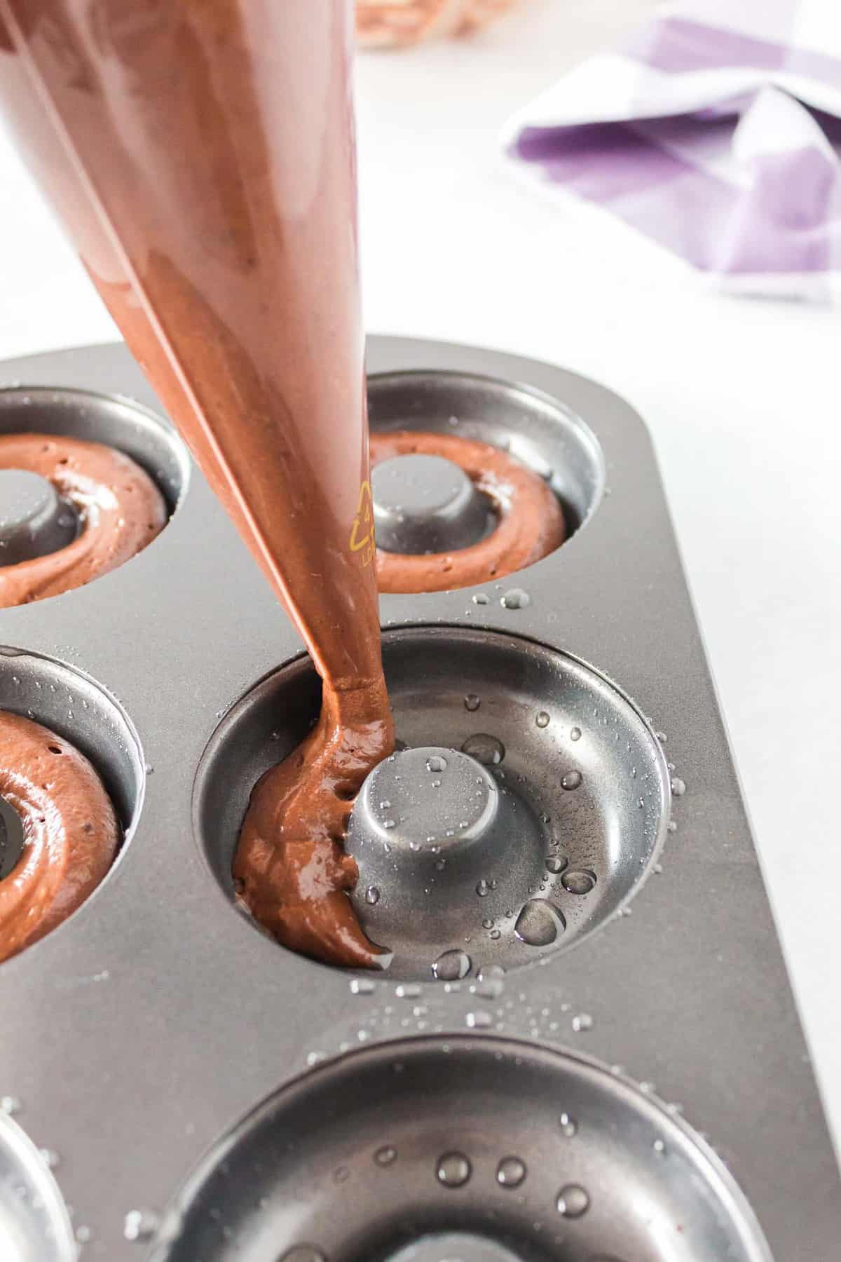Chocolate batter being piped into a donut pan.