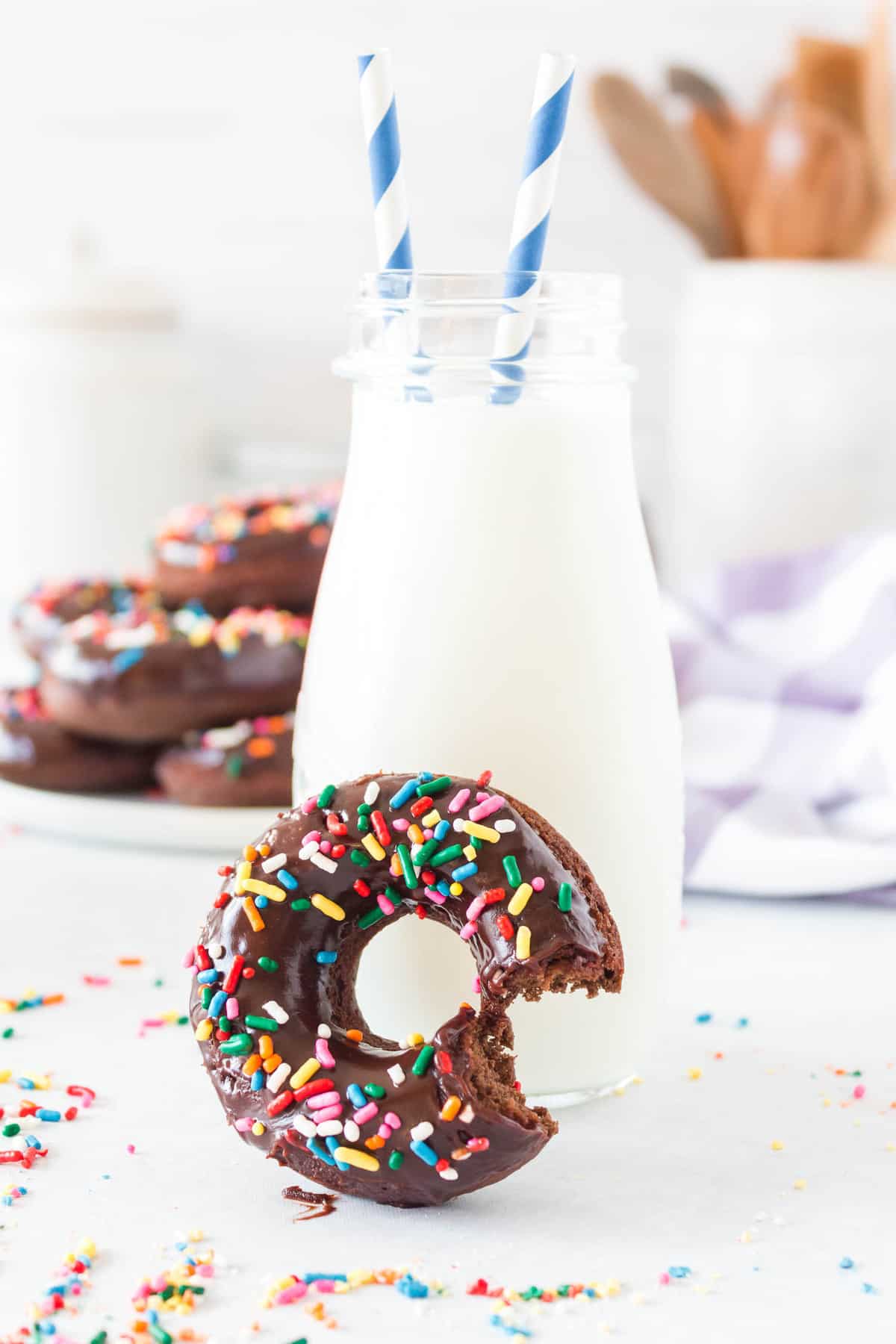 Chocolate sprinkle donut with a bite out of it, in front of a glass bottle of milk.