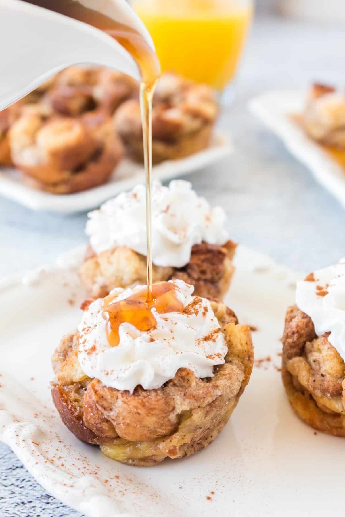 Syrup being poured on a whipped cream topped french toast muffin.