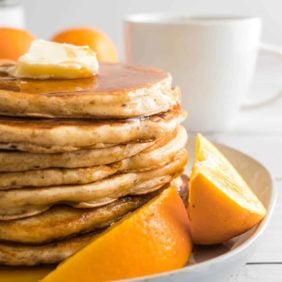 Pancakes stacked on a plate, with orange wedges.