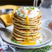Tall stack of pancakes with a runny fried egg on the top.