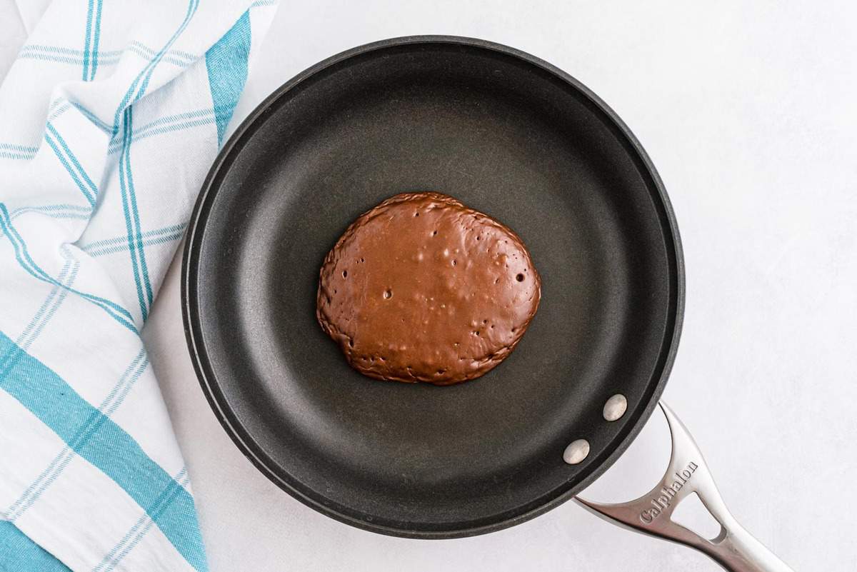 Halfway cooked chocolate pancake in a small black skillet.