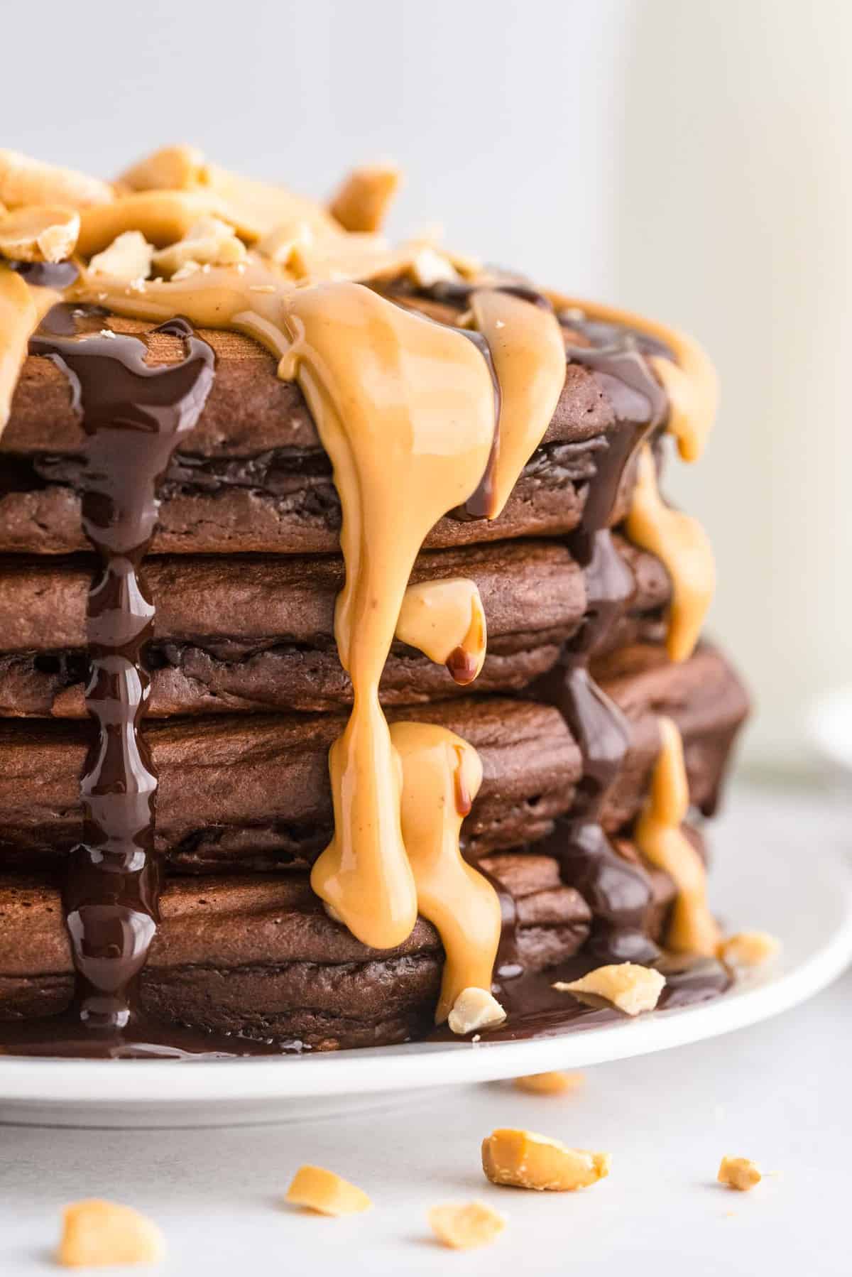 Stack of chocolate peanut butter pancakes with drippy toppings.
