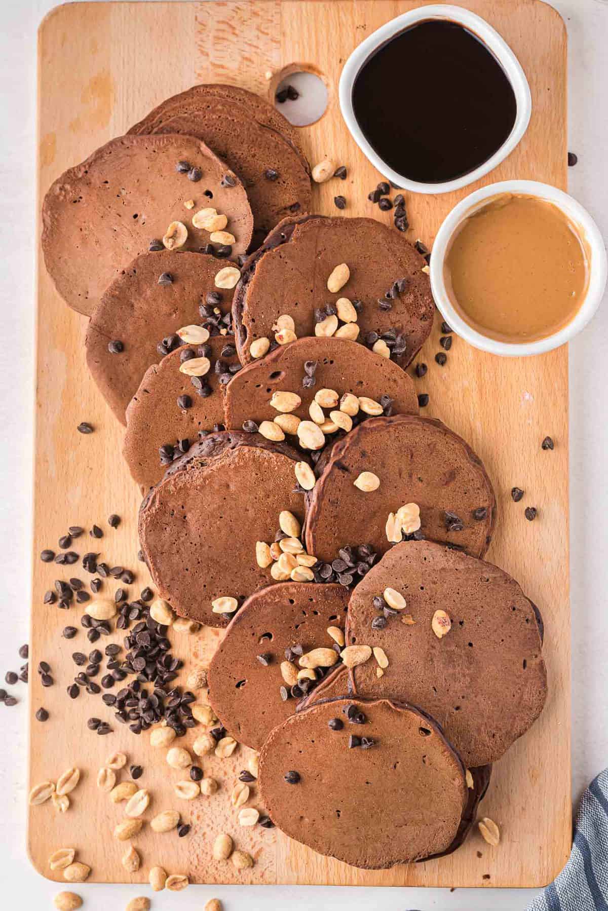 Platter of chocolate pancakes sprinkled with peanuts and chocolate chips.