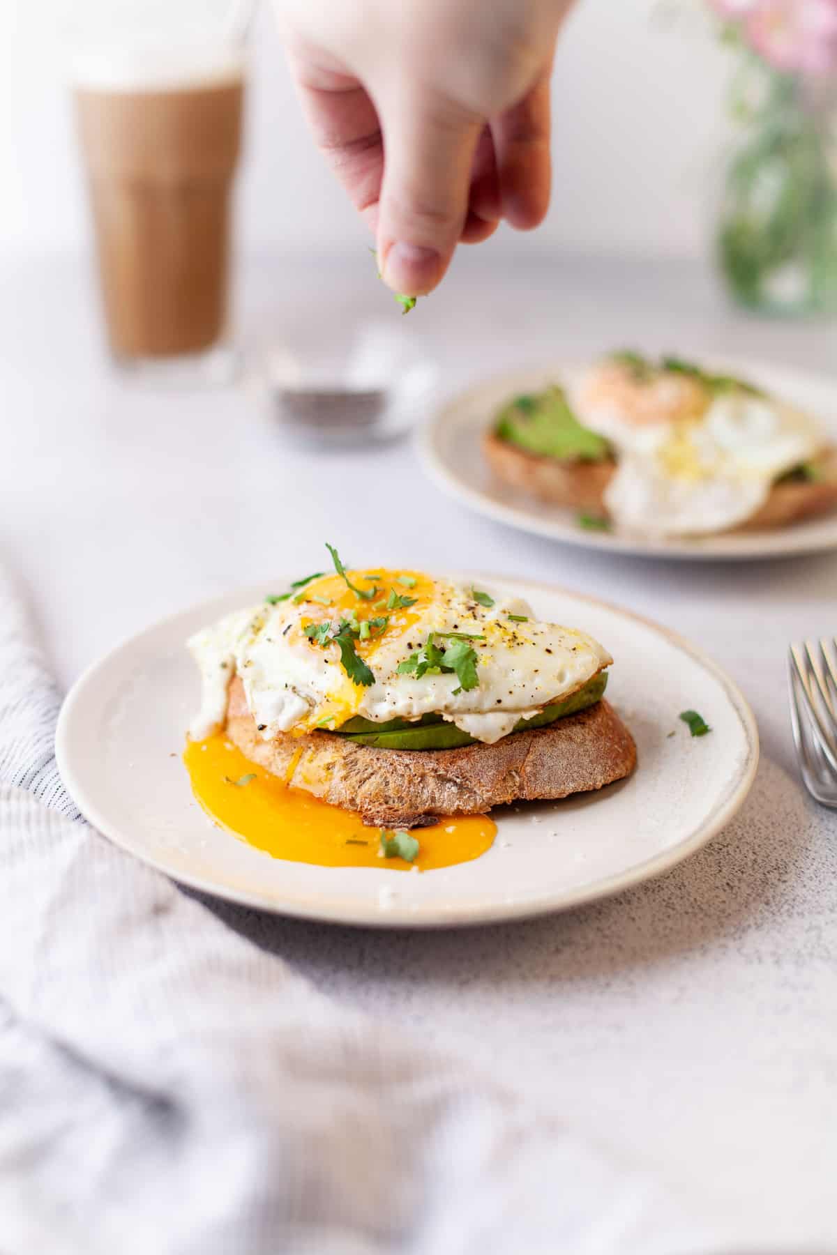 Egg topped avocado toast being sprinkled with herbs.