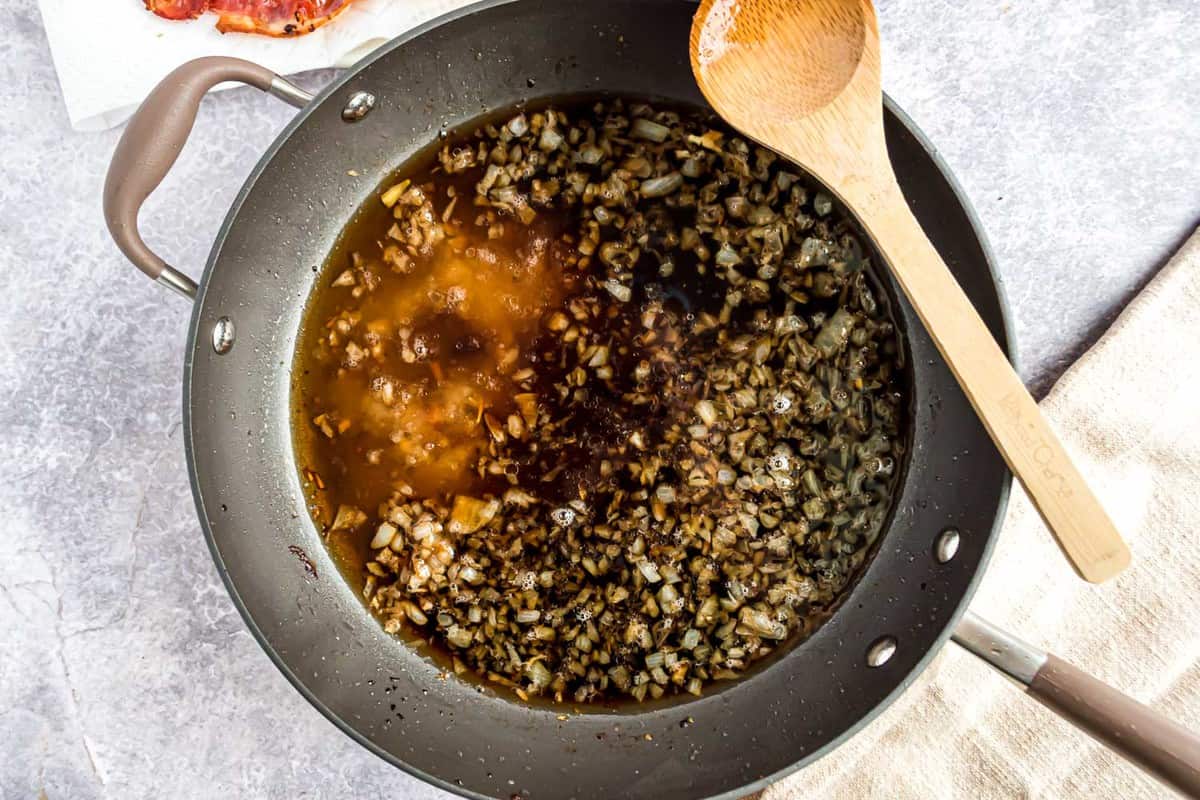 Brown liquid in a black frying pan, wooden spoon resting on side of pan.