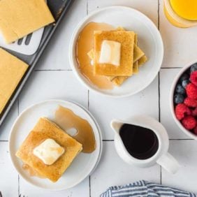 Overhead view of square pancakes on two white plates with syrup and butter.