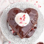 Overhead view of chocolate pancakes in heart shapes, topped with whipped cream and sprinkles.