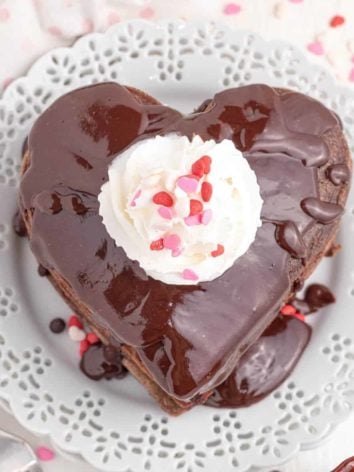 Overhead view of chocolate pancakes in heart shapes, topped with whipped cream and sprinkles.