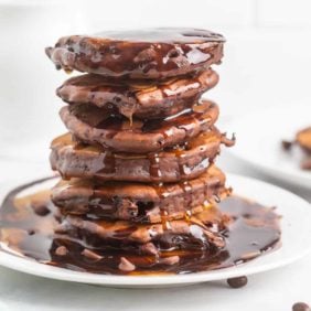 Tall stack of chocolate pancakes with chocolate syrup.
