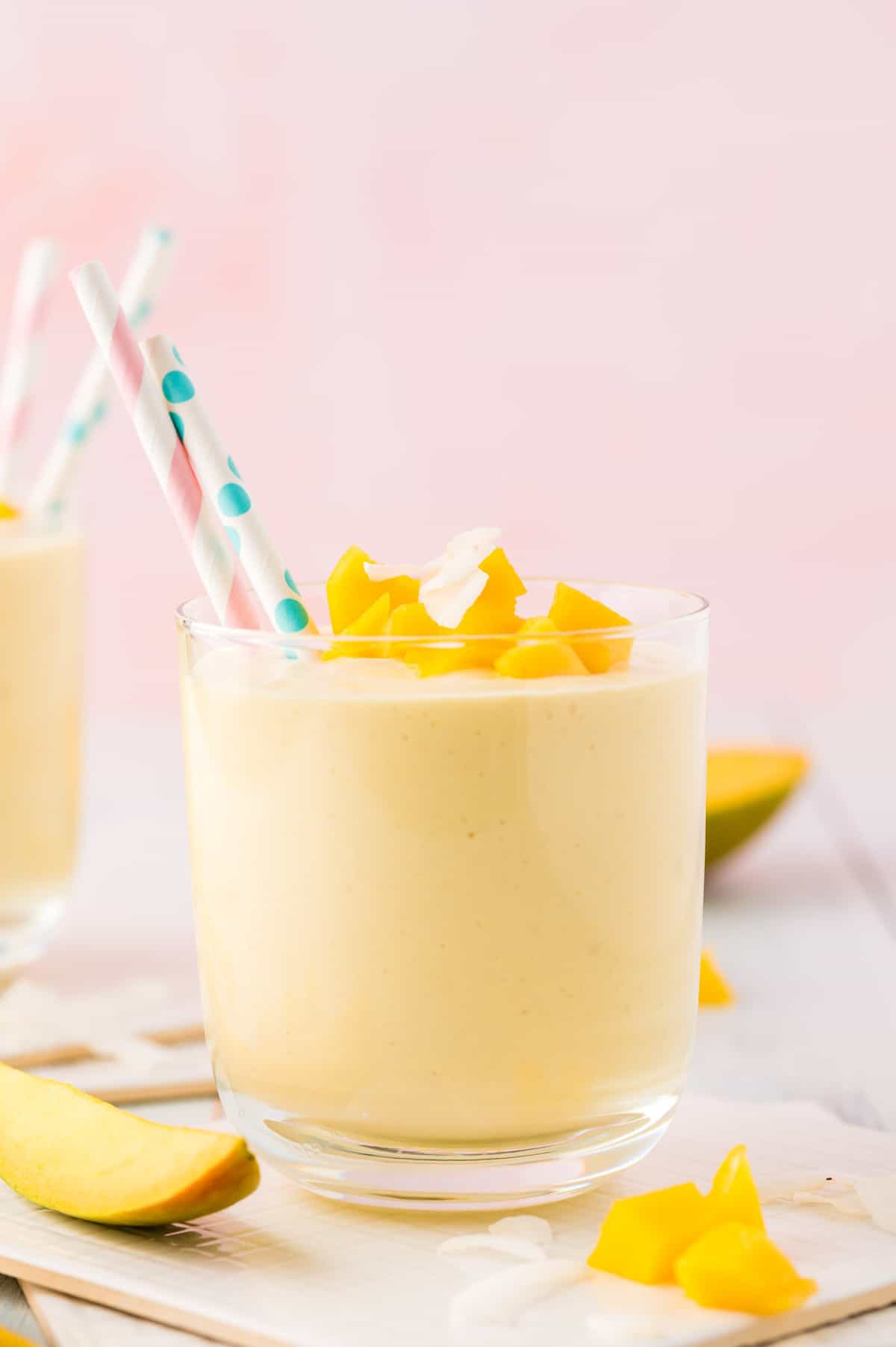 Light orange smoothie in a short glass, topped with fresh mango and coconut.