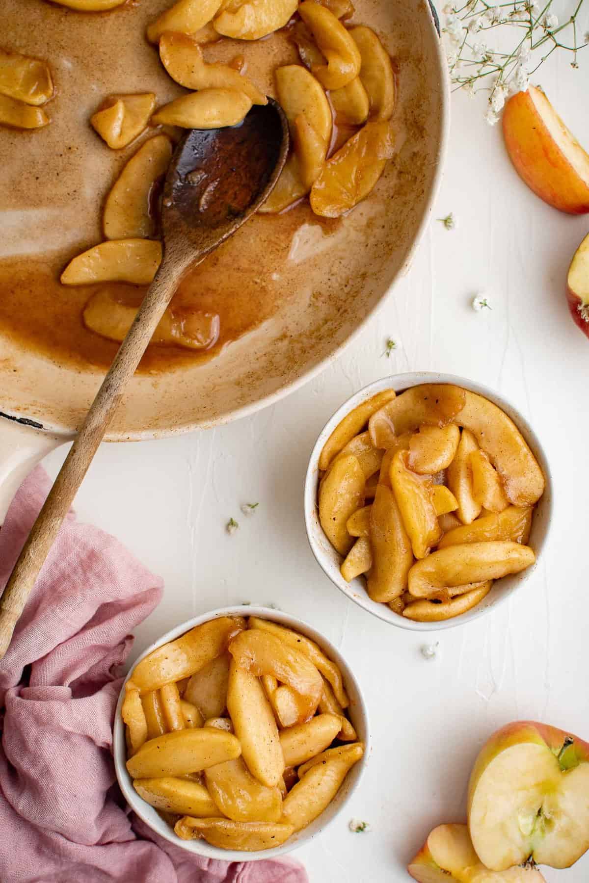 Overhead view of fried apples in two bowls and a frying pan.