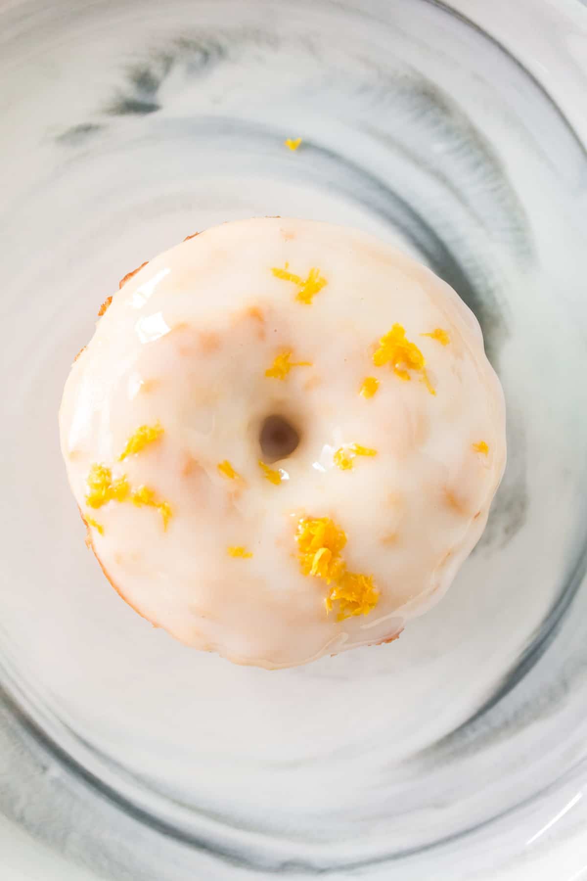 Overhead view of a donut with white frosting and lemon zest.