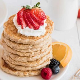Stack of pancakes with whipped cream and strawberries.