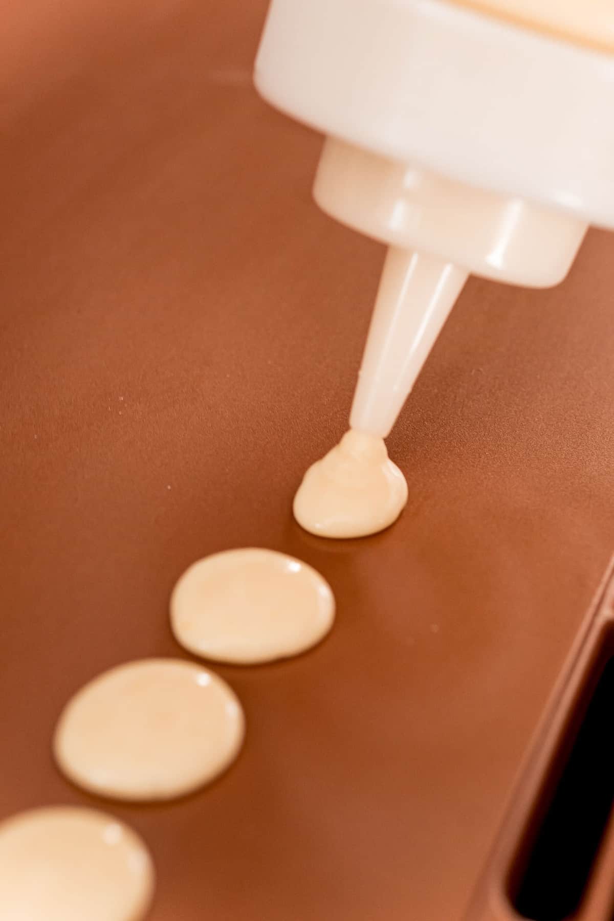 Pancake batter being put on a griddle in small amounts using a squeeze bottle.