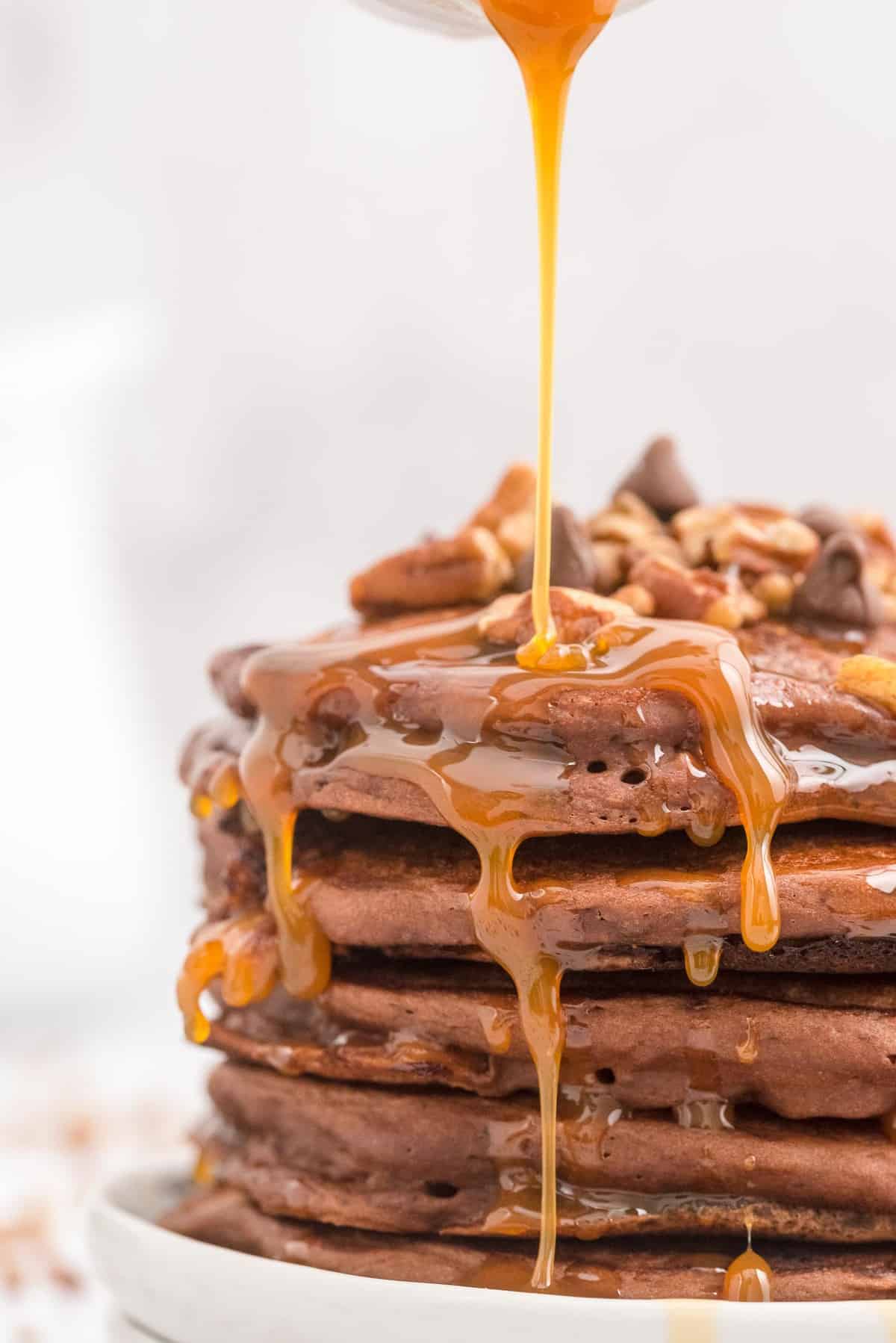 Caramel being poured on a stack of chocolate and caramel pancakes.
