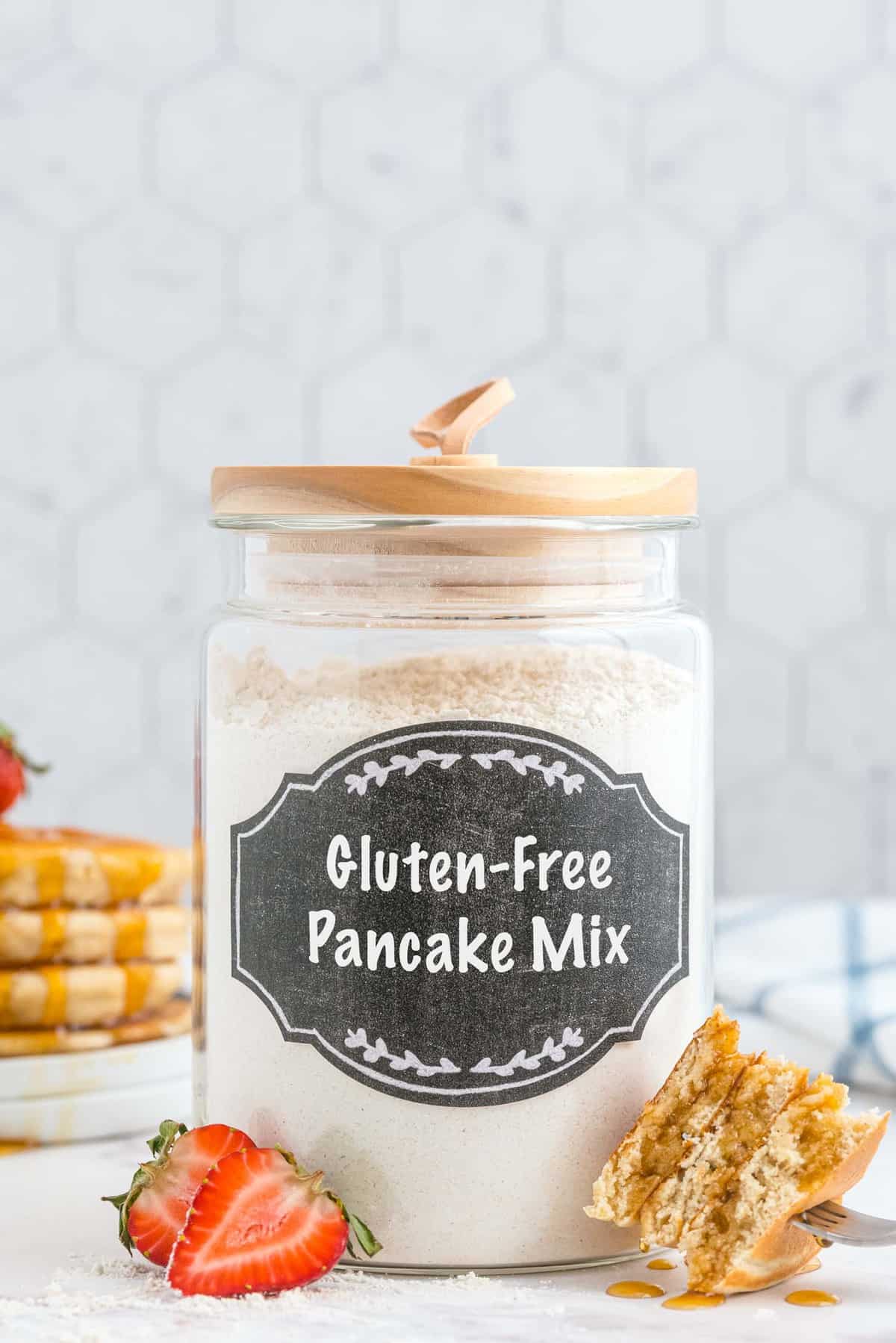 Glass jar with black label that reads "gluten-free pancake mix." Cut pancakes in foreground.
