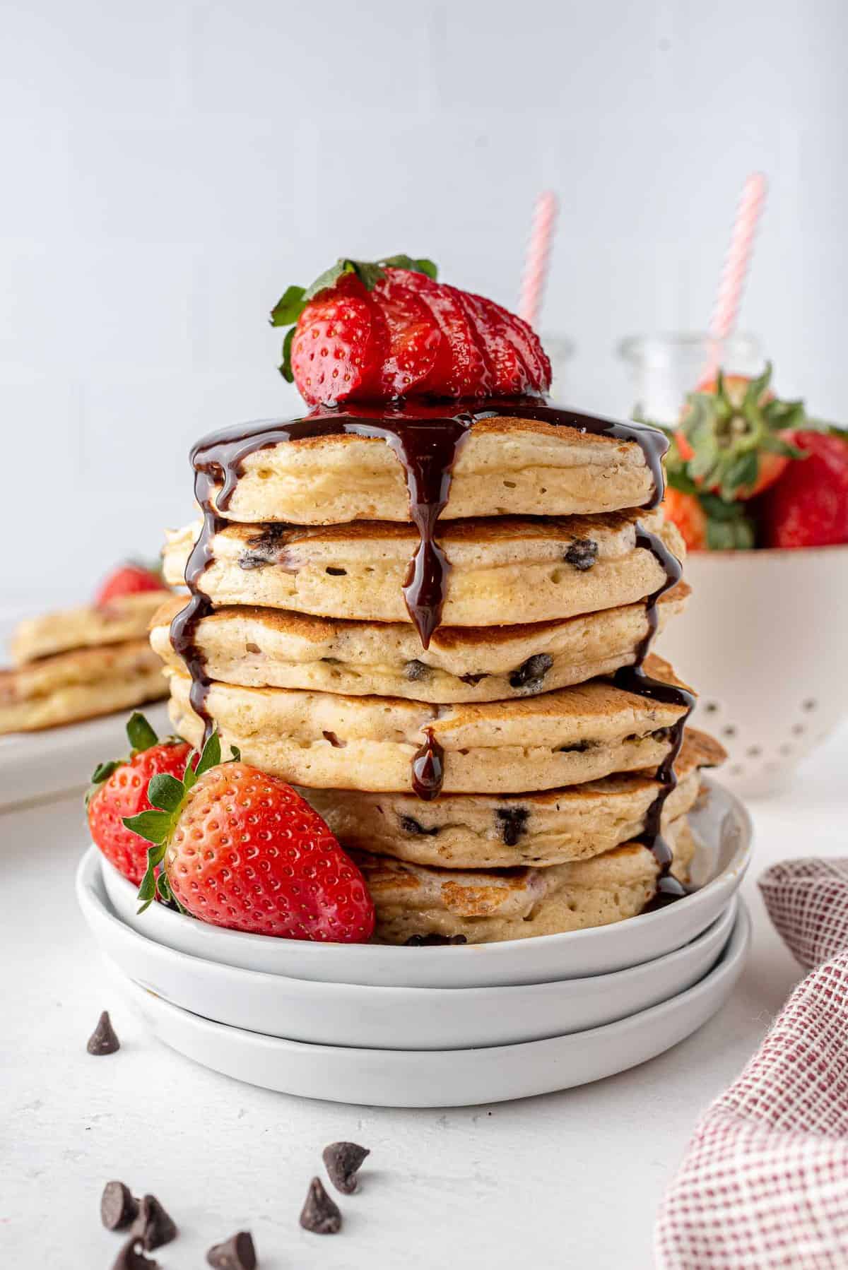 Stack of strawberry chocolate chip buttermilk pancakes topped with chocolate syrup.