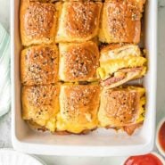 Sliders in a baking dish, one turned sideways to show filling of eggs, ham, and cheese.