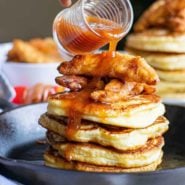 Maple syrup and sriracha being poured on a stack of pancakes with fried chicken.