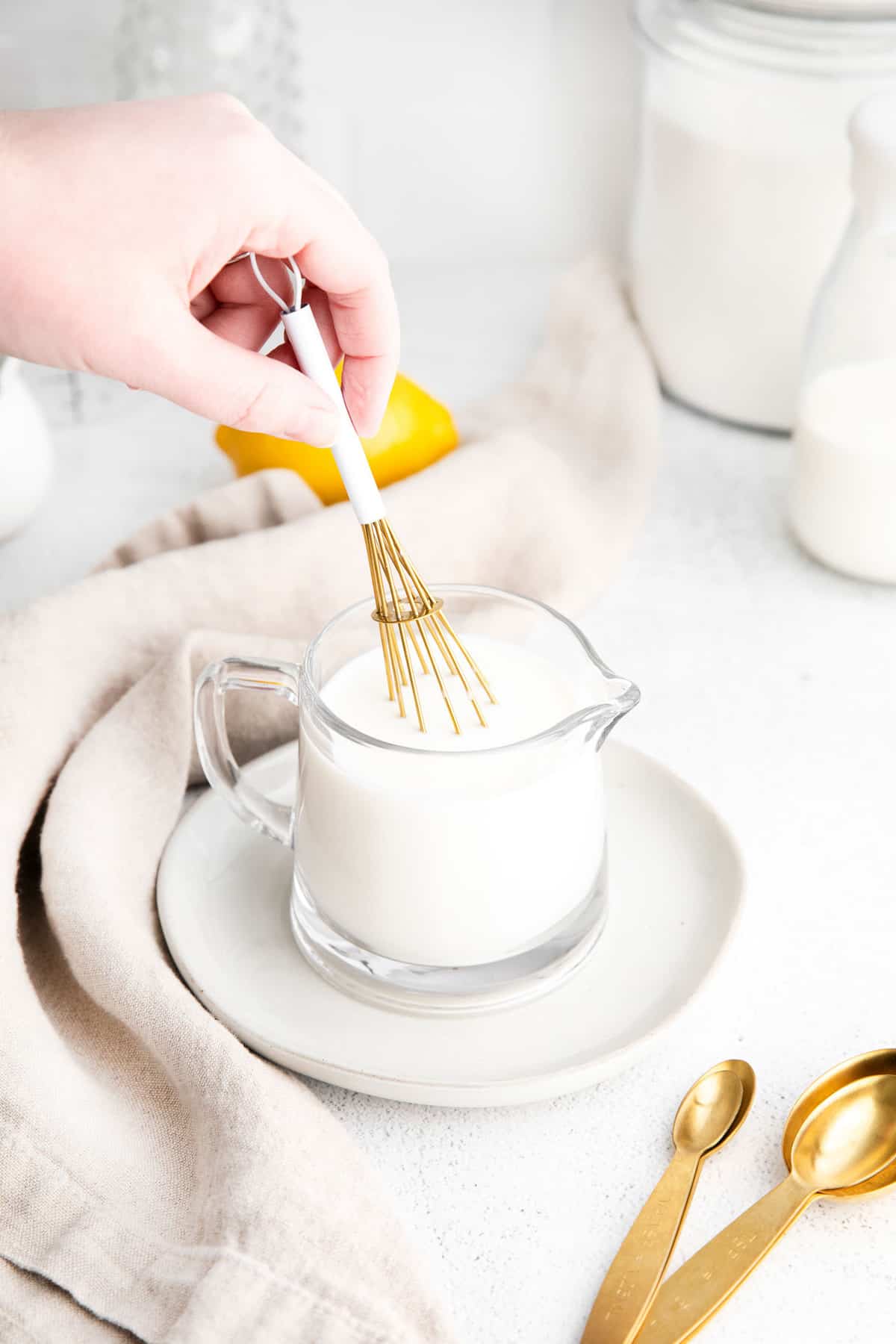 Small glass pitcher of milk, with a hand whisking it with a small whisk.