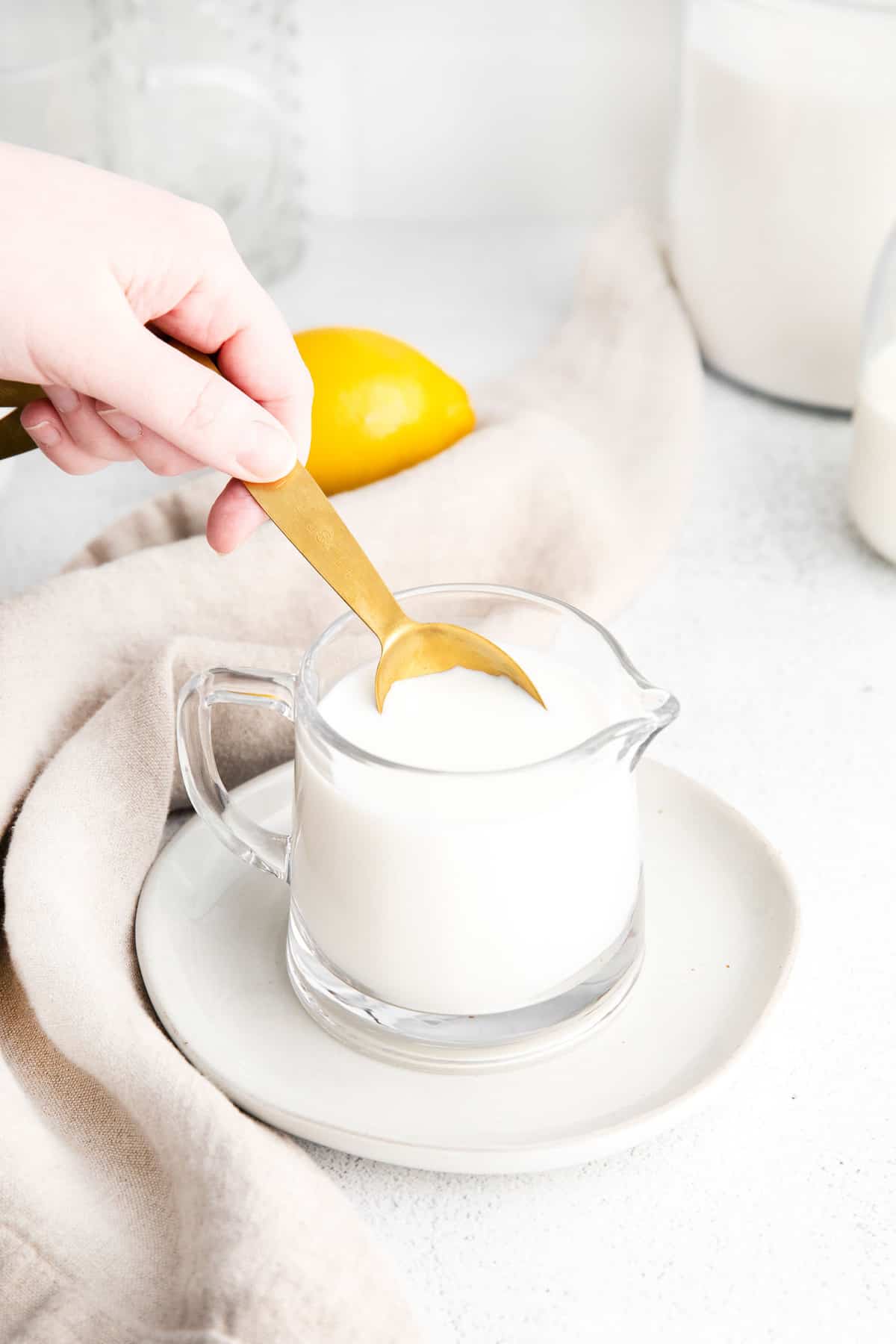 Measuring spoon being dipped into a small glass pitcher of milk.