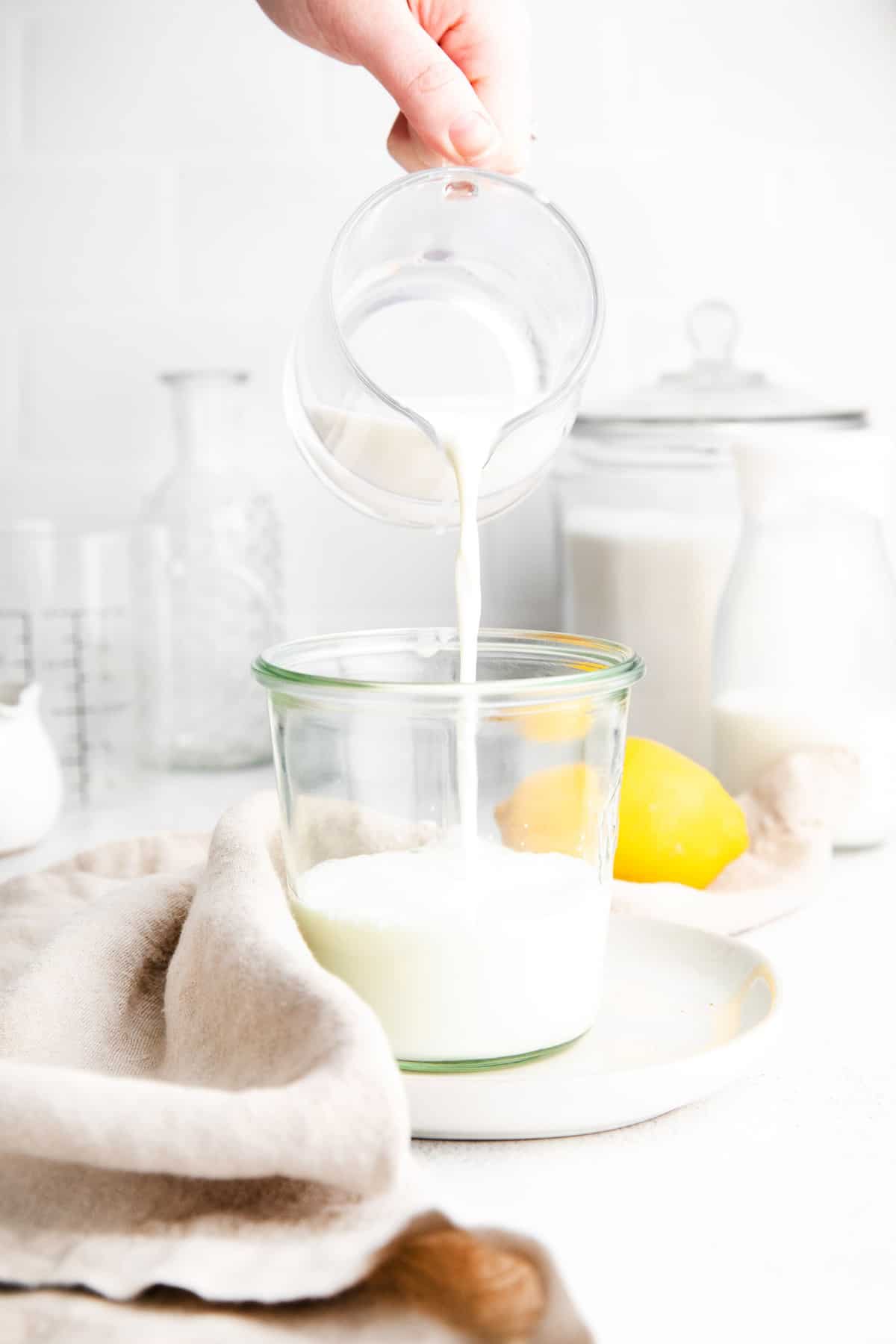Buttermilk being poured from a small glass pitcher into a little jar.