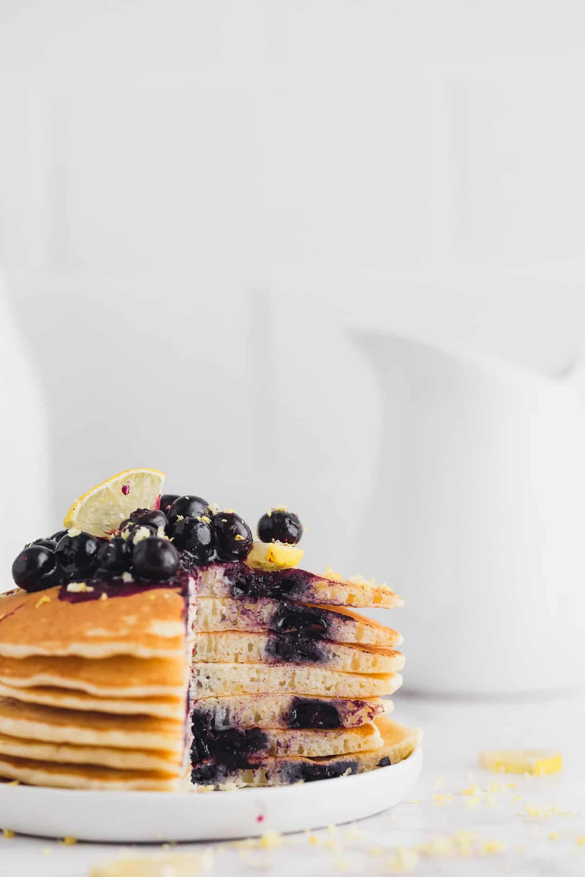 Stack of lemon blueberry pancakes with a slice cut out, blueberry sauce dripping down.