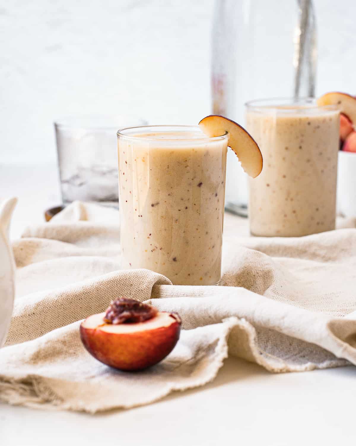 Two light orange-ish brown smoothies garnished with nectarine slices.