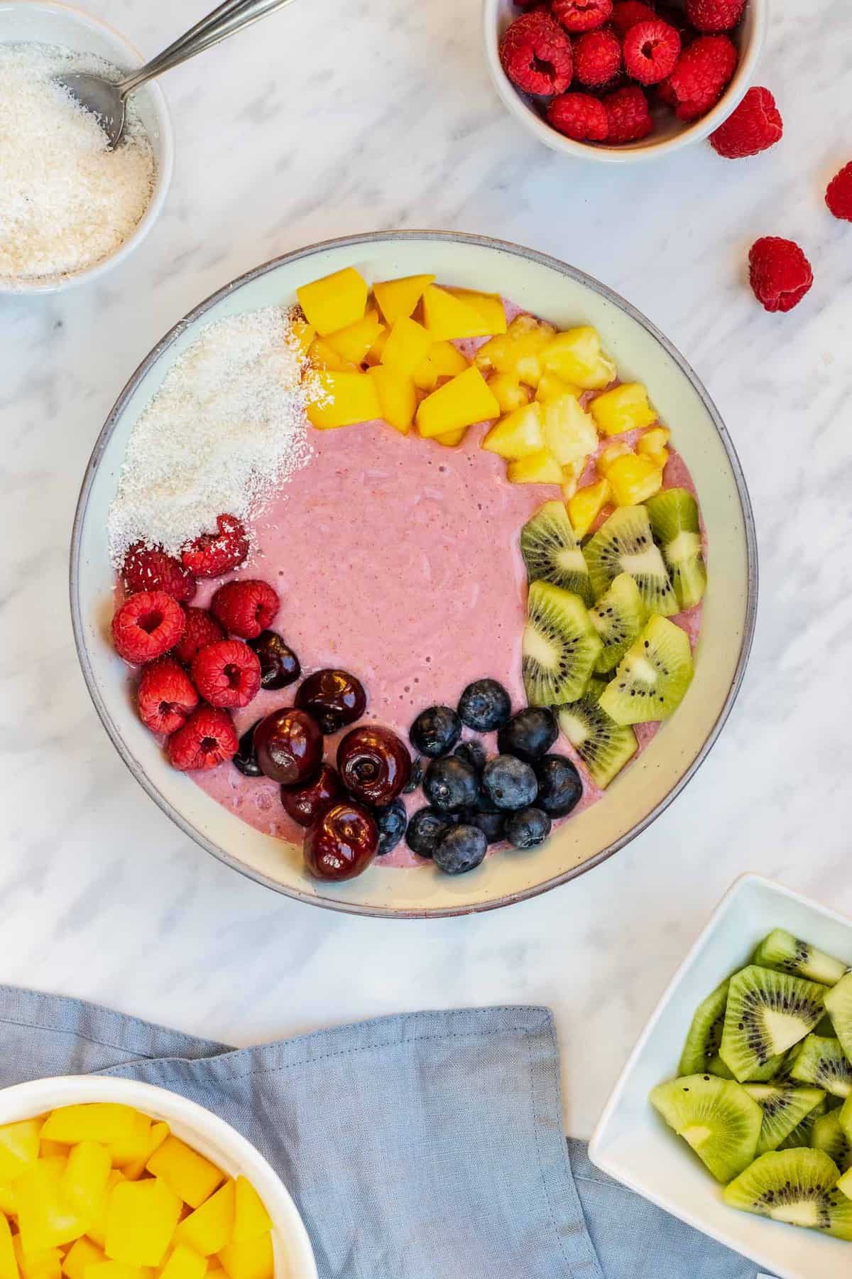 Rainbow smoothie bowl surrounded by toppings.