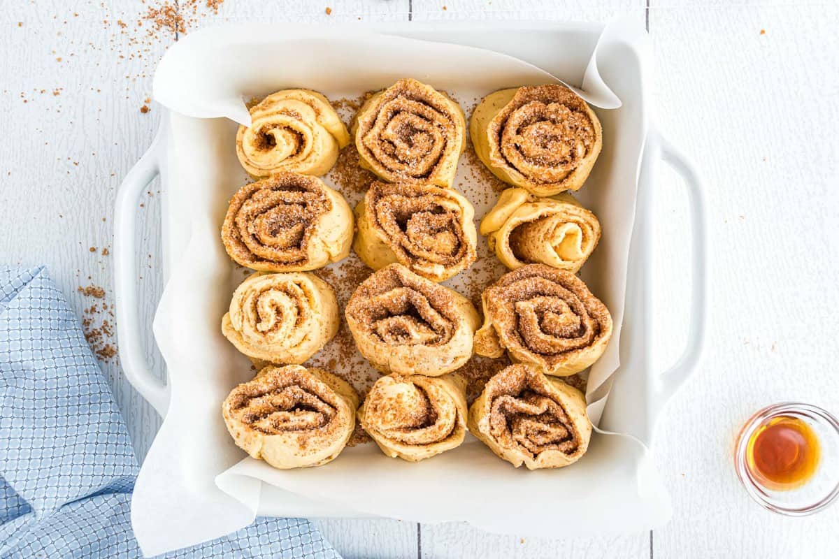 Cinnamon rolls unbaked in a square baking dish.