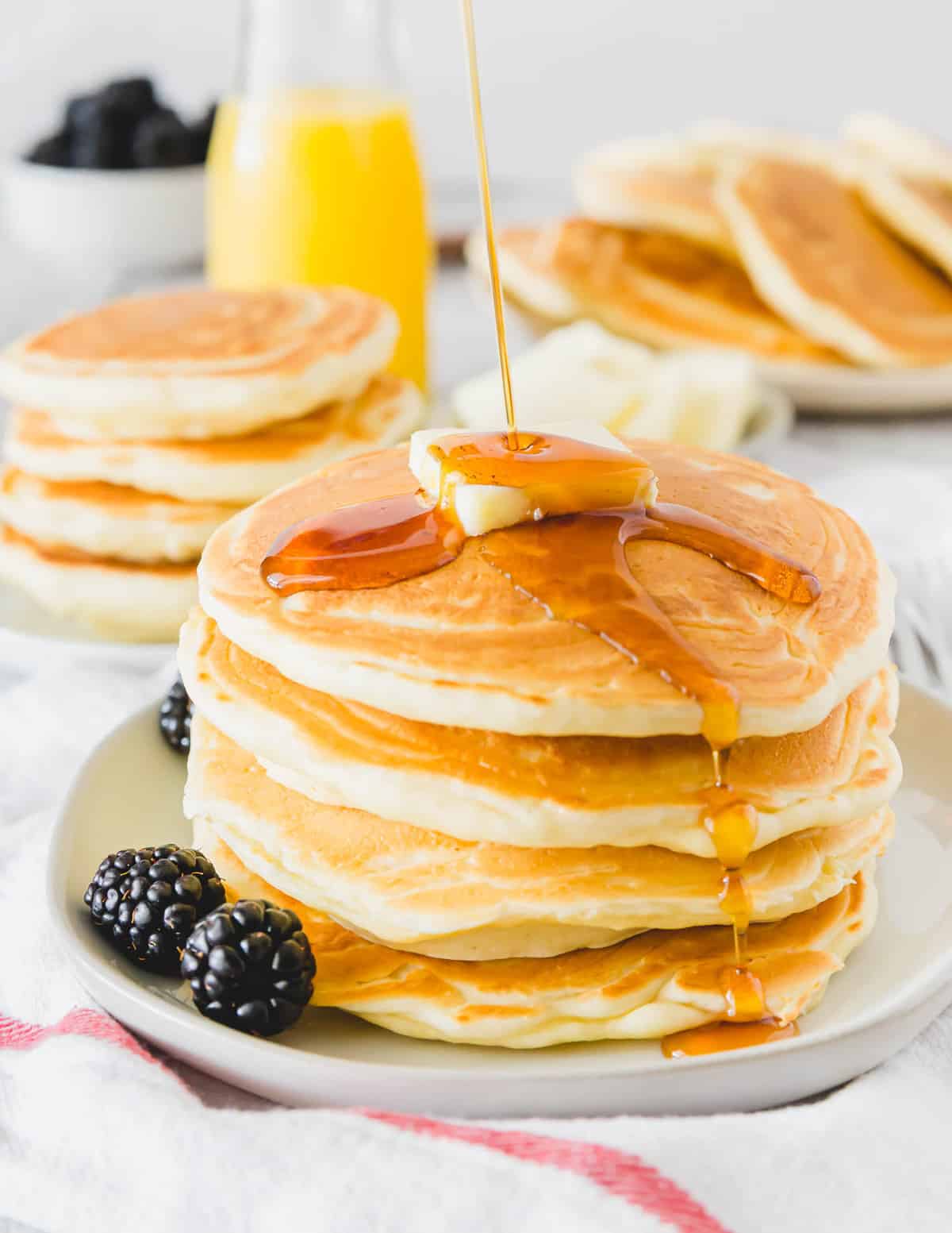 Syrup being poured on a stack of fluffy pancakes.