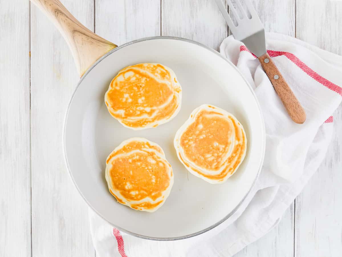 Cooked pancakes in a white frying pan.