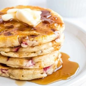 A stack of strawberry flecked pancakes topped with butter and syrup.
