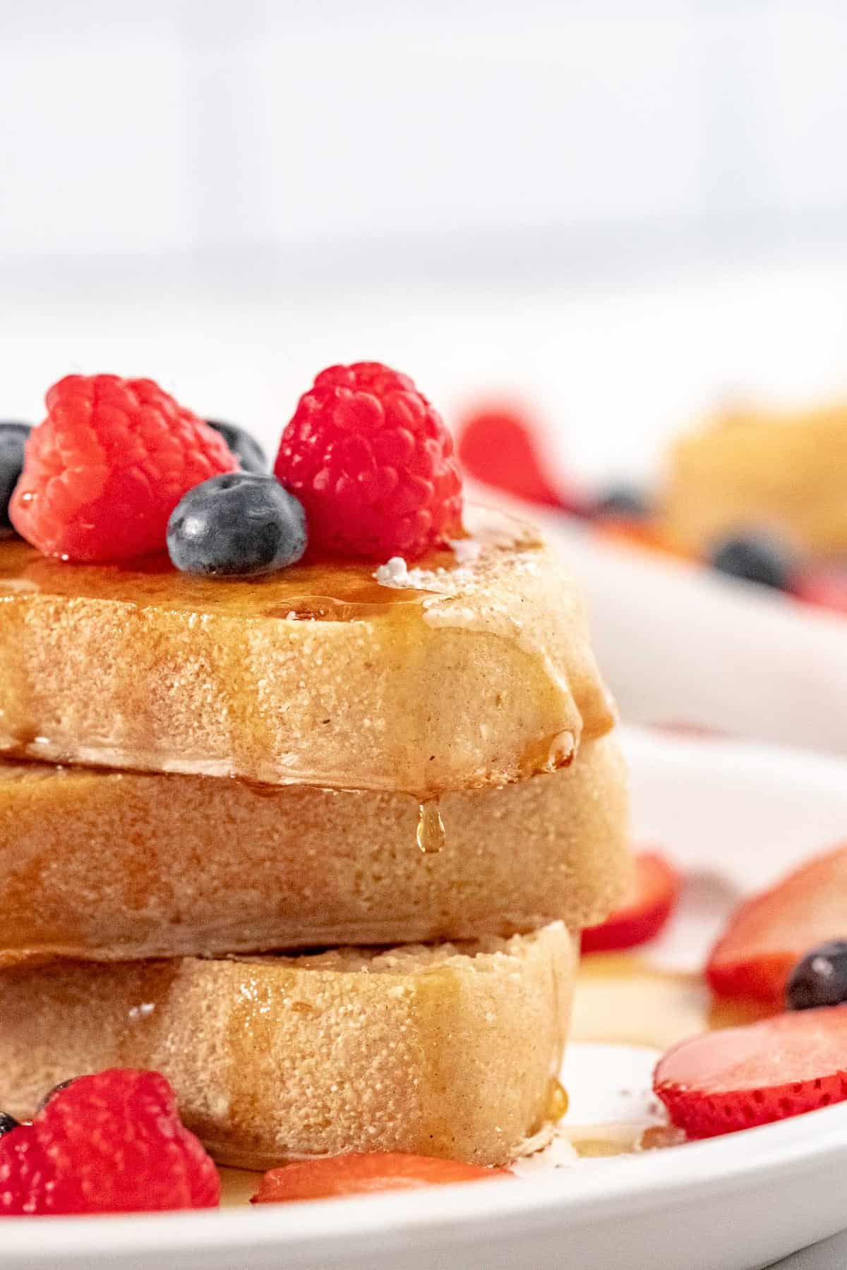 Close up of stack of three slices of french toast dripping with syrup.
