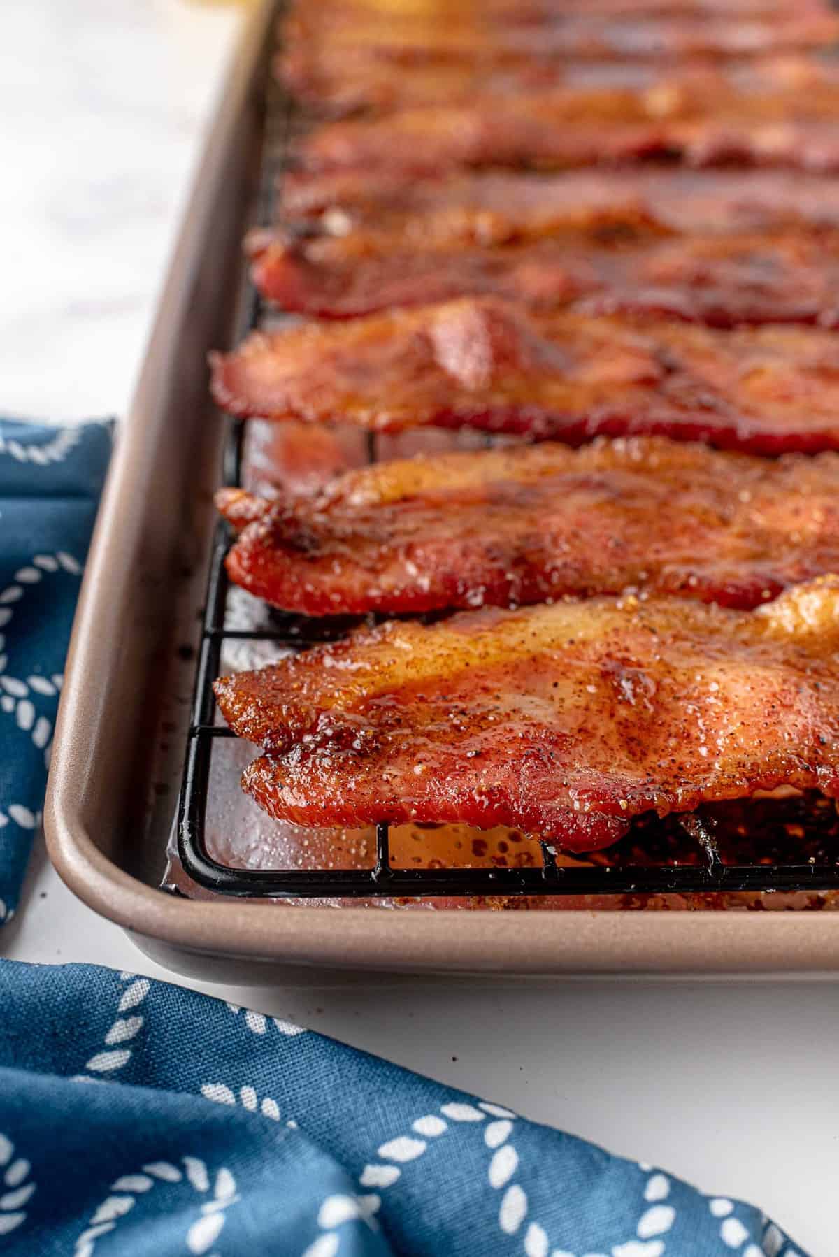 Close up of bacon that has been candied and cooked, on a wire rack inside a sheet pan.