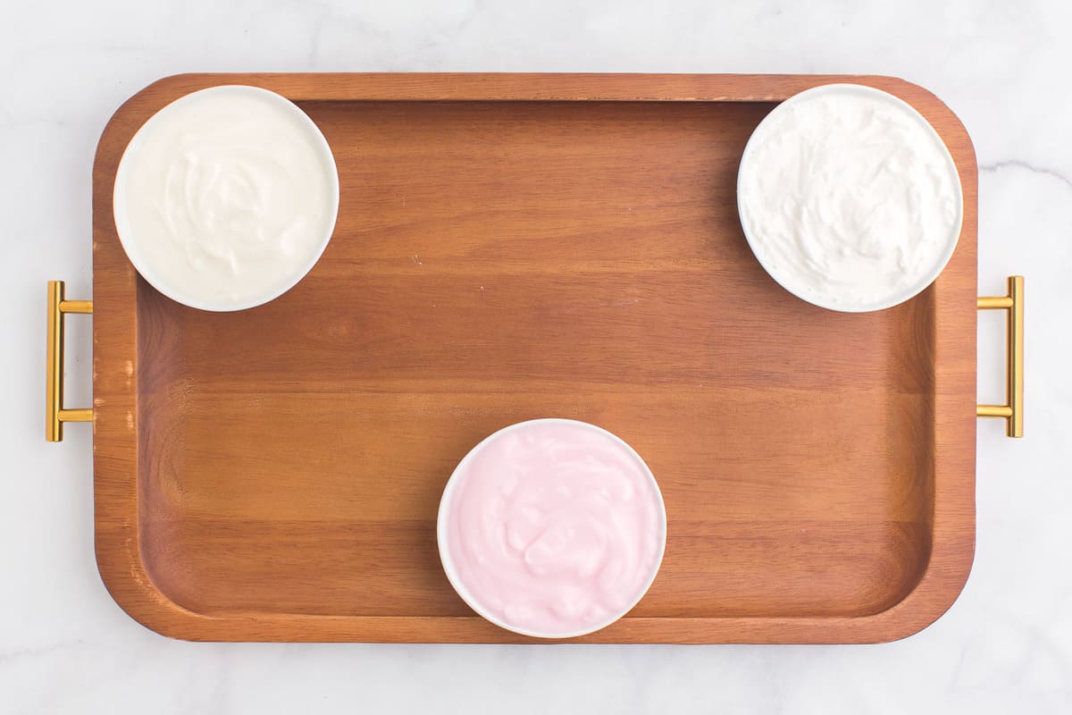 Three bowls of yogurt on a wooden board.