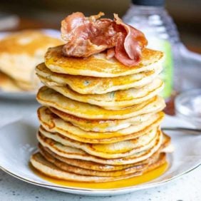 Tall stack of pancakes topped with bacon.