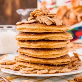 Tall stack of pancakes topped with cinnamon toast crunch cereal.